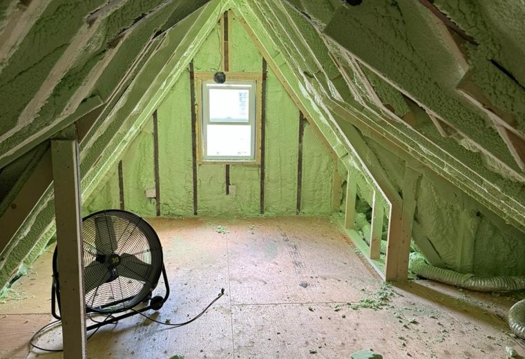Exposed attic framing with spray equipment staged on the floor