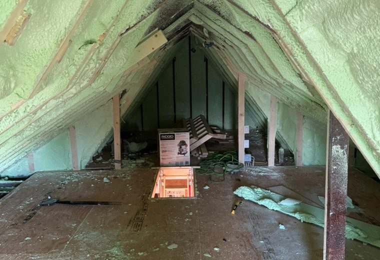 Gray spray-applied material covering the rafters and roof deck of an attic